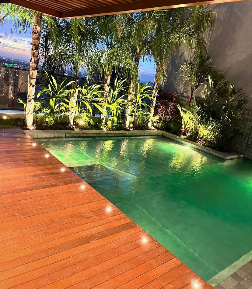 Área externa com deck, paisagismo e piscina iluminada